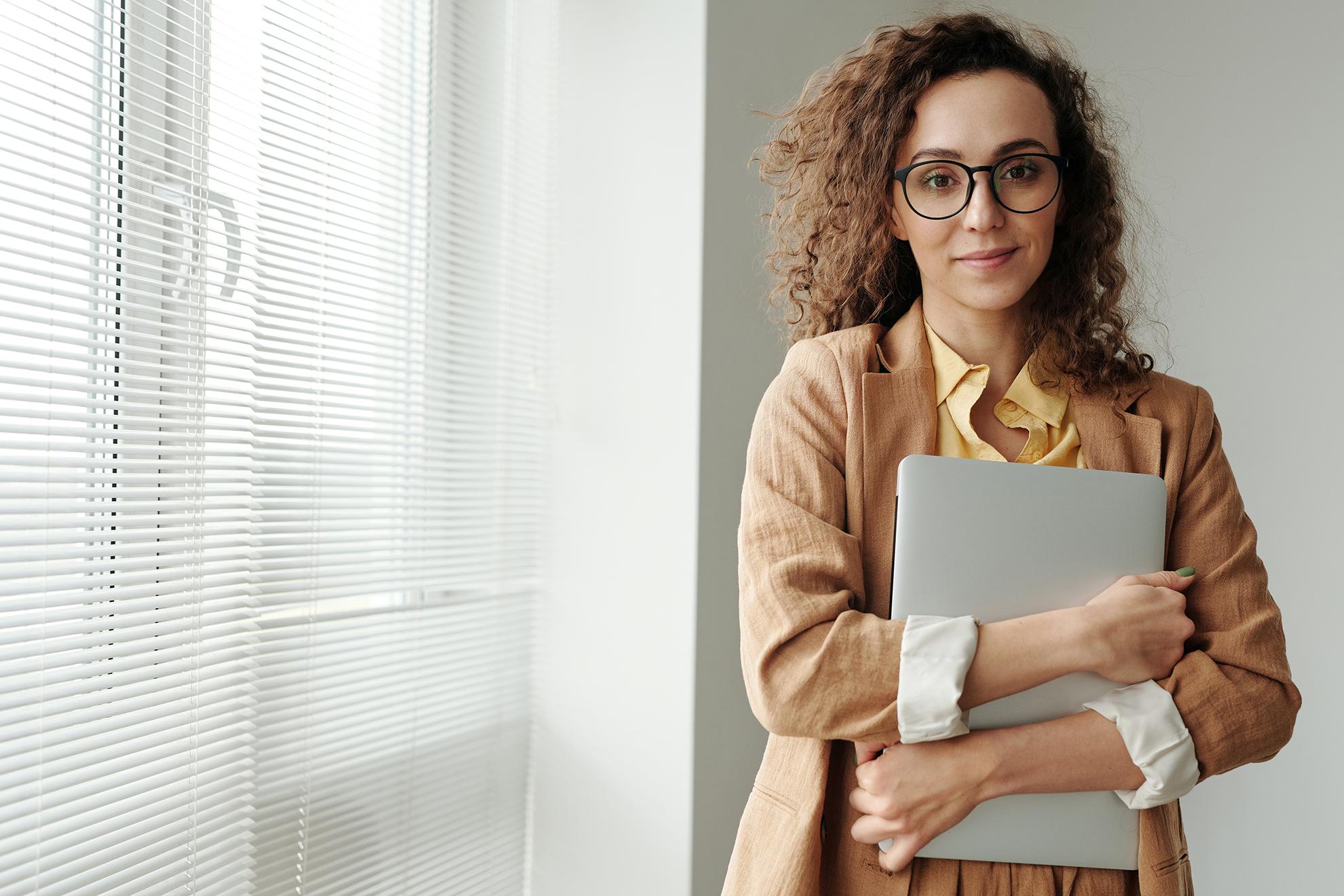 A picture of a woman with eyeglasses holding a laptop